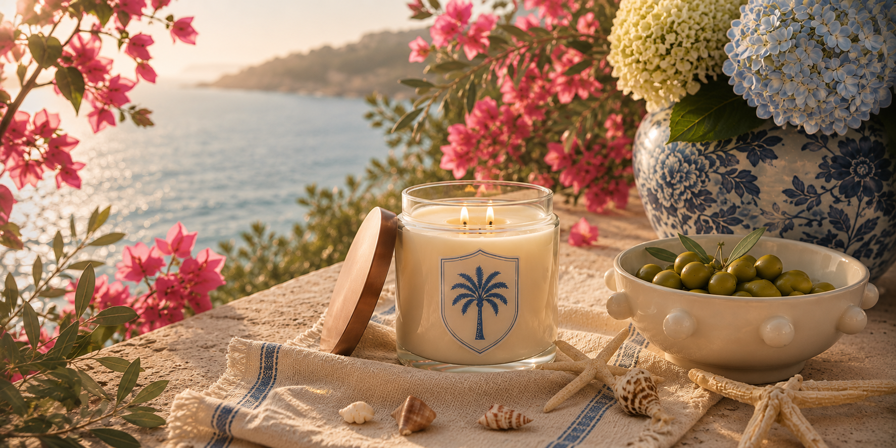 Coastal Tile Society candle on a linen-draped seaside table with olives, shells, and hydrangeas