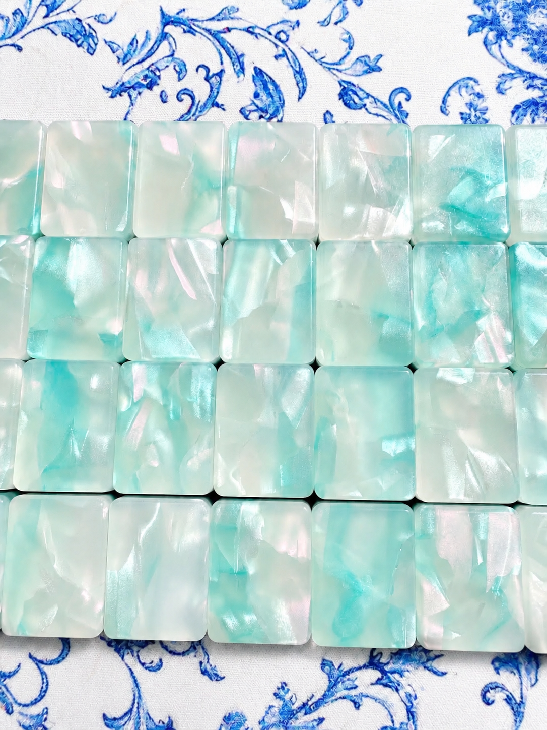 Coastal Tile Society tile backs in pearlescent aqua marbled acrylic arranged in rows on a blue-and-white floral mat